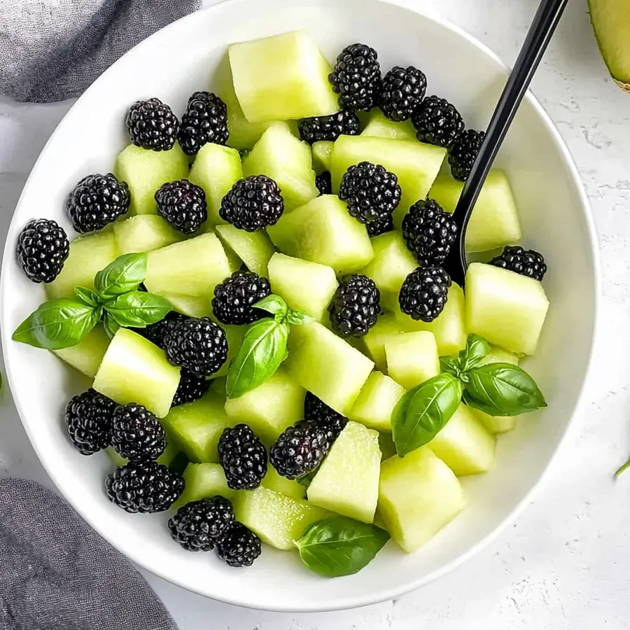 Un bol de ensalada de frutas con moras, melón verde y albahaca.