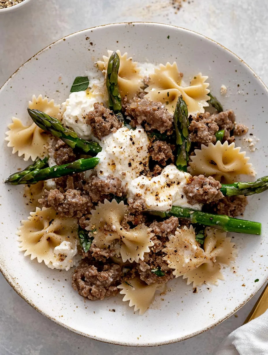Un plato de comida con pasta, salchicha y espárragos.