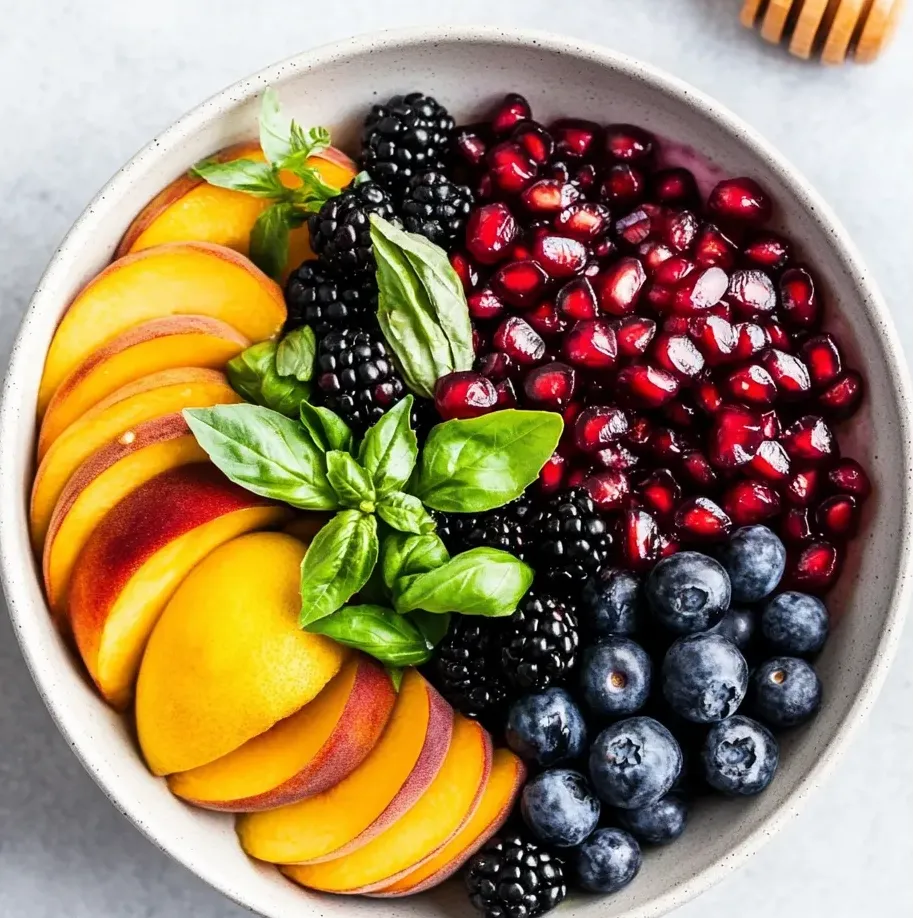 Un bol de fruta con arándanos, moras, melocotones y miel.