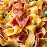 Un plato de pasta con jamón y guisantes.