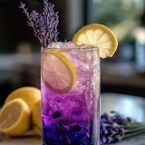 Vaso de bebida morada con rodajas de limón y lavanda.
