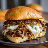 Un pan con queso derretido, cebolla y carne jugosa servido en un plato.
